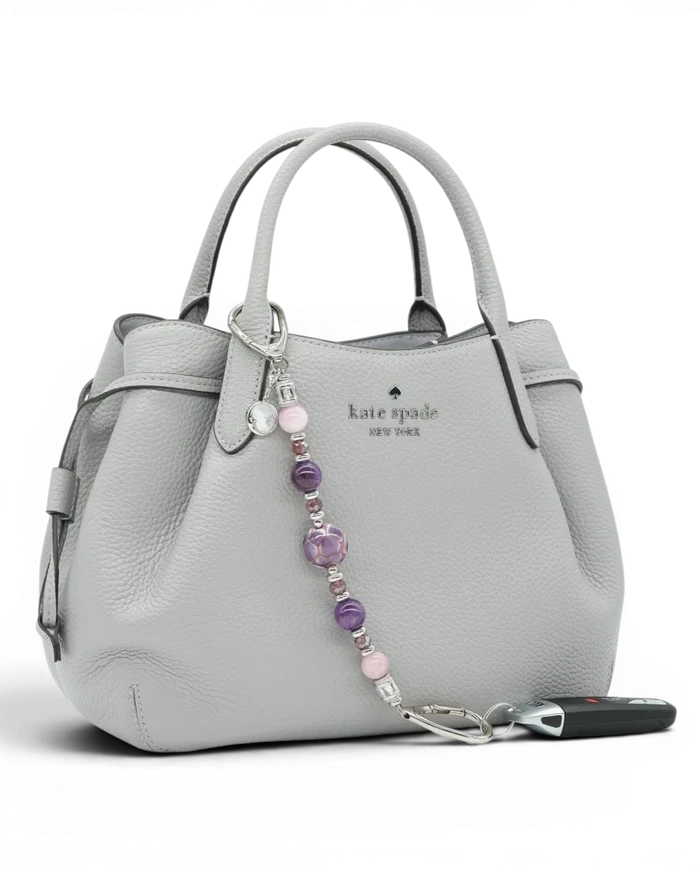 LD Keyfinder Amethyst Moon keychain with amethyst, kunzite, and glass beads, and a moon charm on a grey handbag.