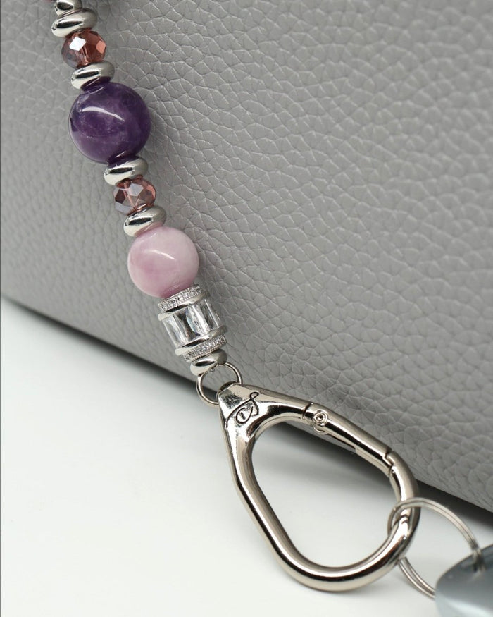 LD Keyfinder Amethyst Moon key finder with amethyst, kunzite, glass beads, and moon charm attached to a grey leather bag.
