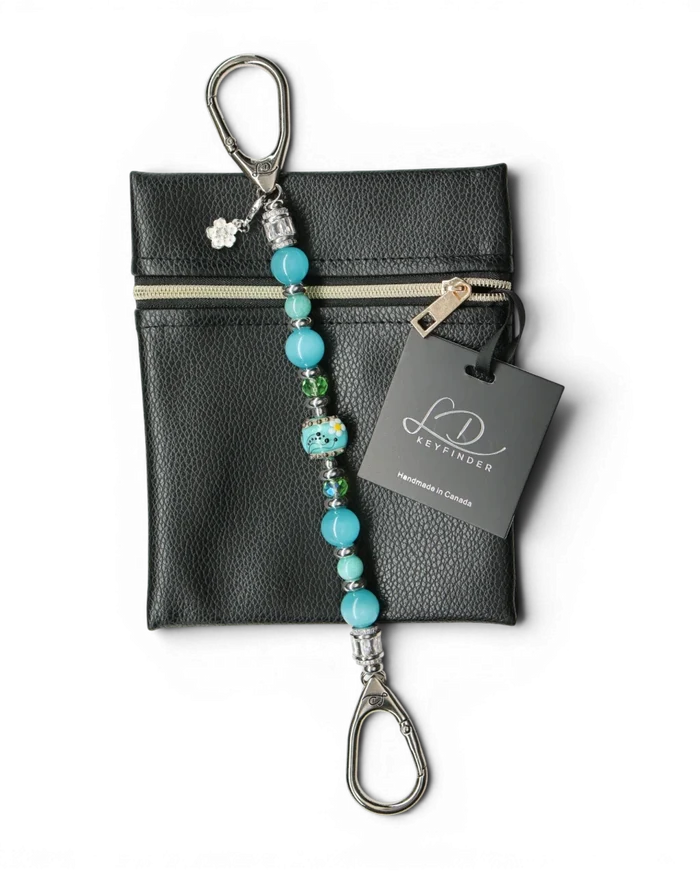 LD Keyfinder Azure Meadow keychain with aqua blue Amazonite beads, green glass beads, and a central lampwork glass bead with white daisies. Includes a black pouch.