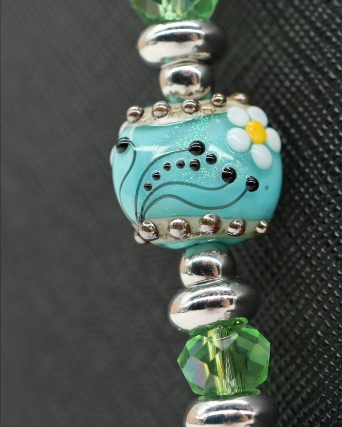 LD Keyfinder Azure Meadow bracelet with aqua blue cat's eye beads, green faceted glass beads, and a central lampwork glass bead with a daisy.