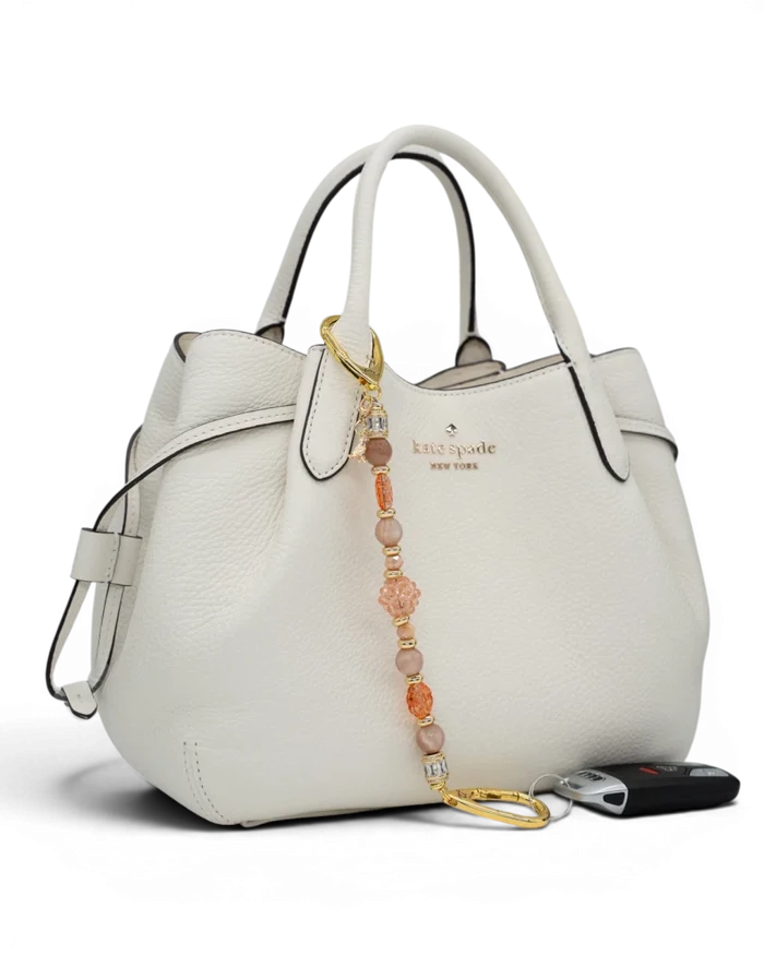 LD Keyfinder Birdsong Bliss beaded accessory with sunstone, coral flower, and gold bird charm attached to a white handbag.