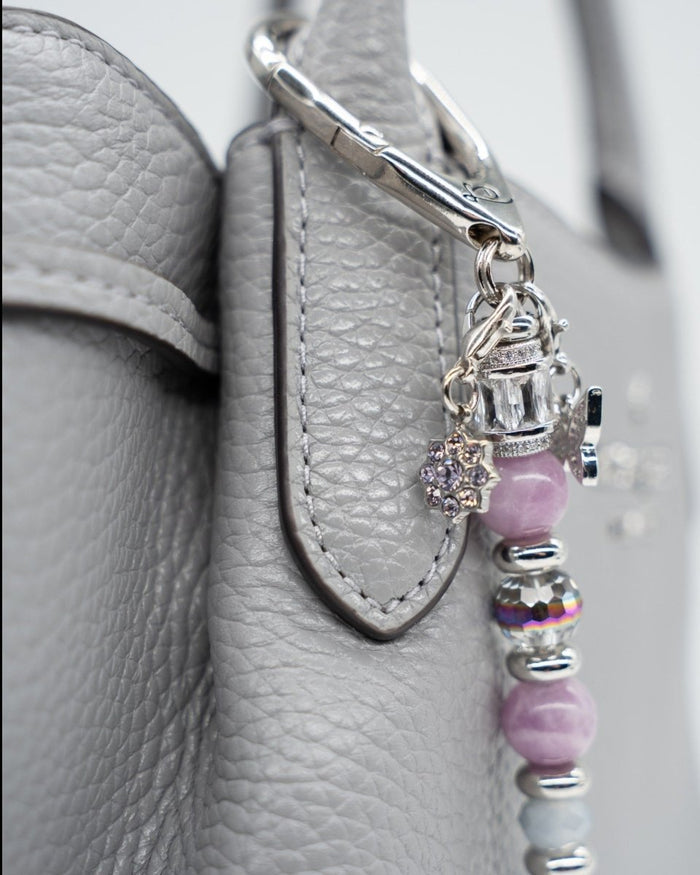 LD Keyfinder Blooming Joy accessory featuring lavender Lepidolite, purple Jade, and artisan glass tulip on a grey bag