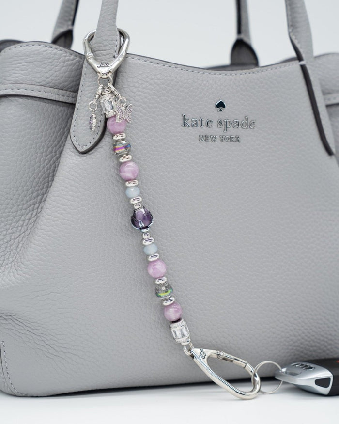 LD Keyfinder Blooming Joy beaded keychain with Lepidolite, purple Jade, and artisan glass tulip on a grey handbag.