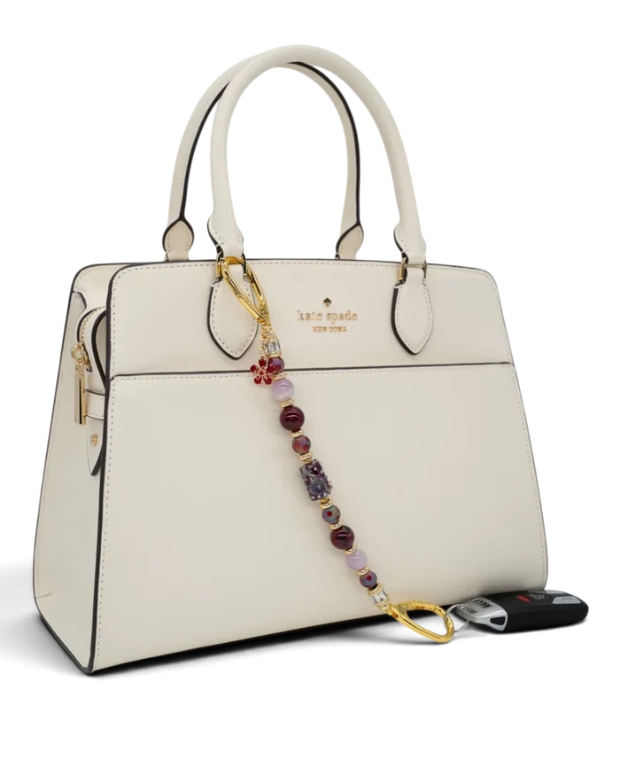 LD Keyfinder Bordeaux Bloom beaded accessory with burgundy agate, lavender kunzite, and gold flower charm on a handbag