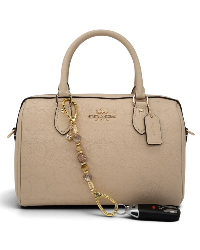 LD Keyfinder Caramel Latte-Mini beaded accessory with tiger eye and gold charms attached to a beige Coach handbag.
