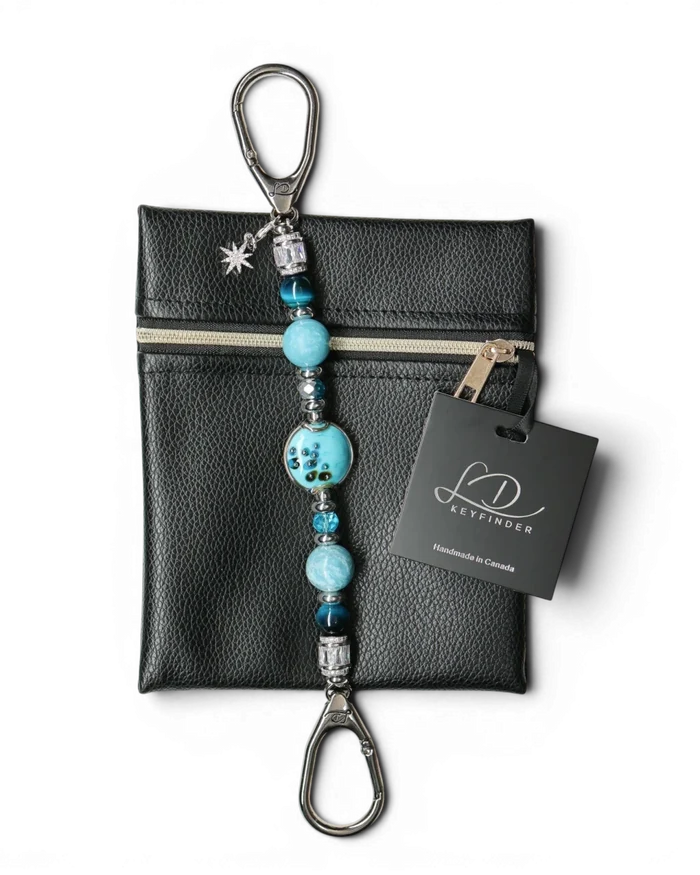 LD Keyfinder Celestial Tide keychain with turquoise glass bead, blue tiger eye, larimar, and silver accents, attached to a black pouch.