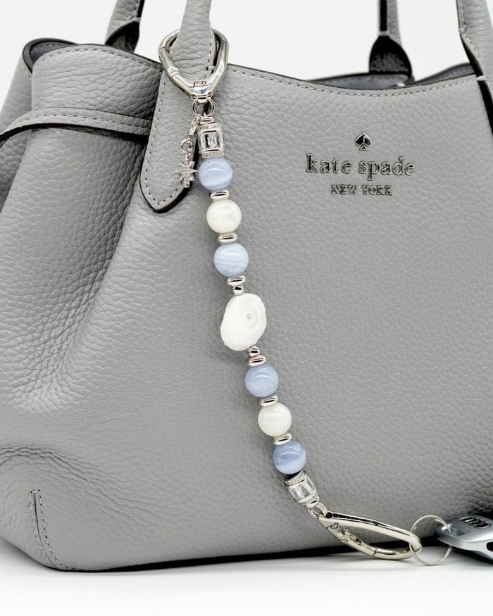 LD Keyfinder Cloud Dancer accessory with blue lace agate, moonstone, and a star charm attached to a grey handbag.