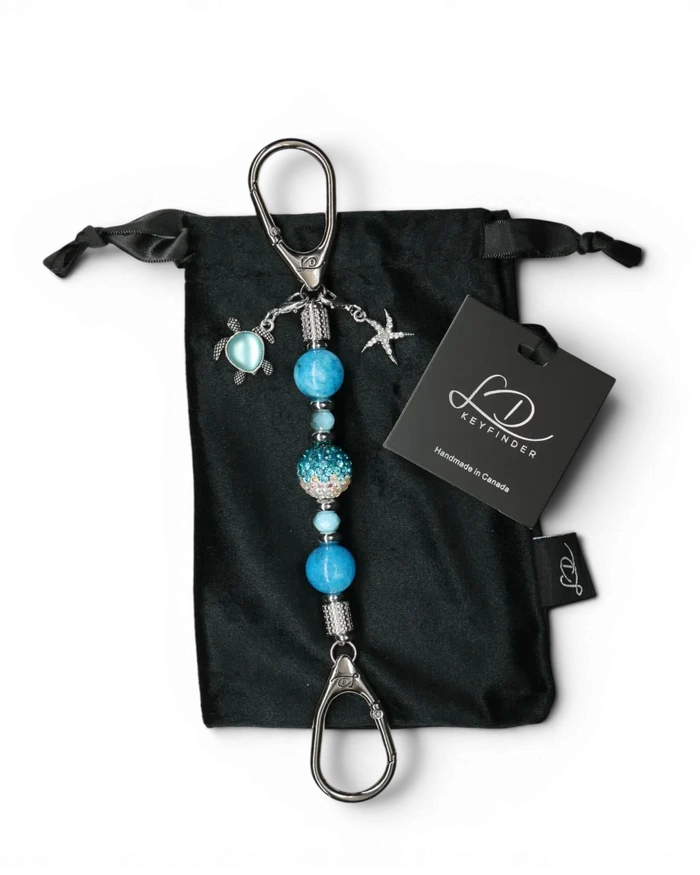 LD Keyfinder Coastal Tide Mini keychain with blue gemstone beads, crystal bead, turtle and starfish charms on black velvet pouch.