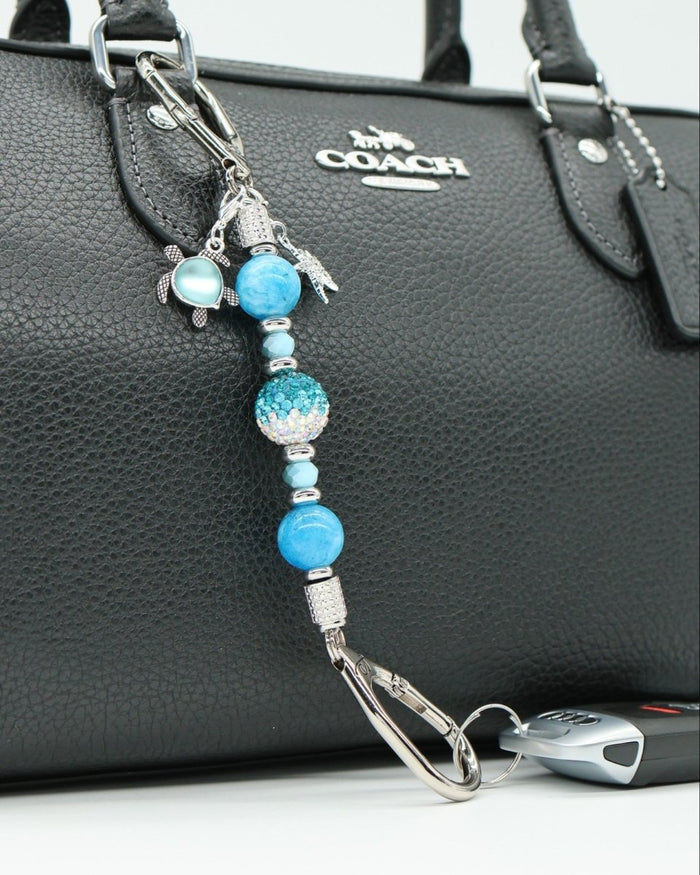 LD Keyfinder Coastal Tide Mini keychain with blue gemstone beads, turtle and starfish charms attached to a black handbag.