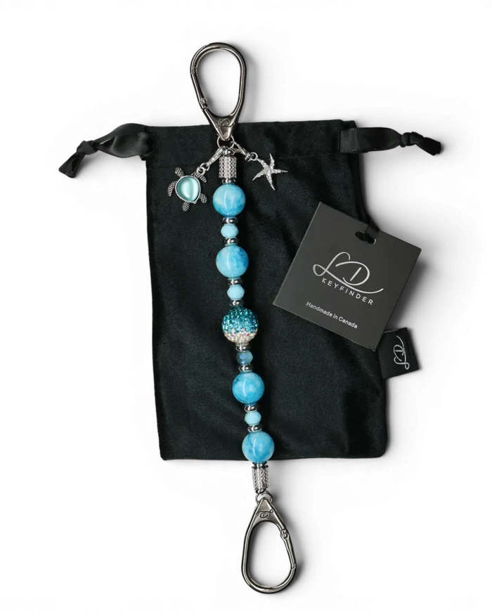 LD Keyfinder Coastal Tide keychain with aqua hemimorphite beads, Austrian crystal, turtle and starfish charms on black velvet bag.