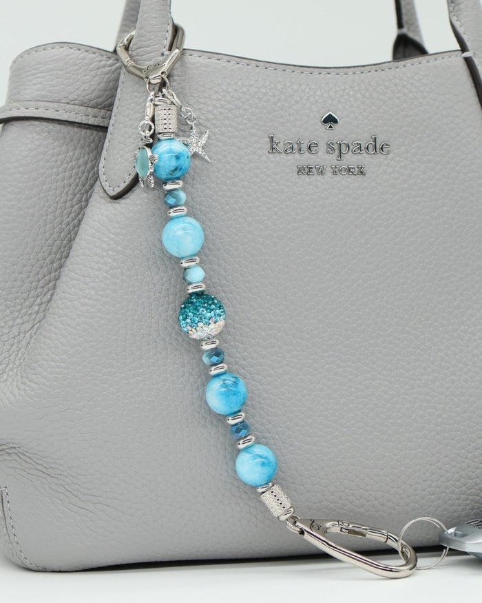 LD Keyfinder Coastal Tide keychain with aqua hemimorphite beads, crystal, turtle and starfish charms on a grey bag.