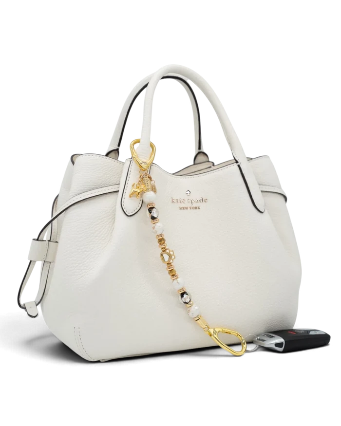LD Keyfinder Furever Love beaded keychain with gold paw charm and white seashell beads attached to a white handbag.