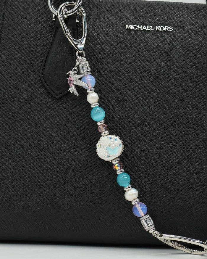 LD Keyfinder Garden Serenade bag charm with pearls, opalite, and artisan clay bead attached to a black handbag.