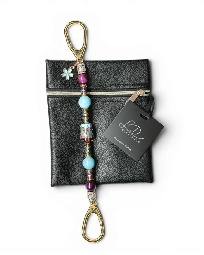 LD Keyfinder Gilded Fantasy keychain with sky blue, topaz, purple tiger eye beads, gold leaf art bead, and blue flower charm on black pouch.