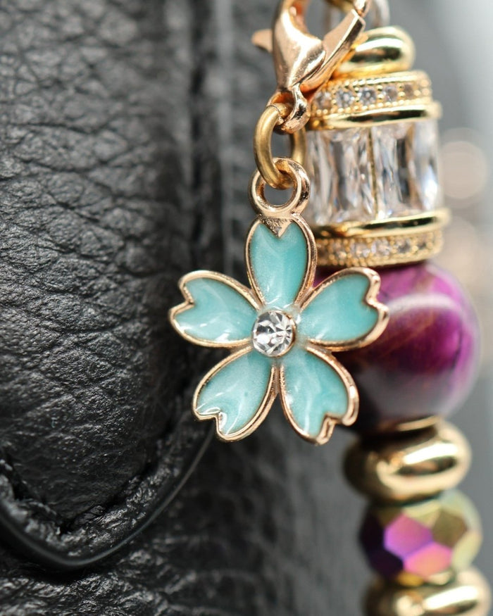 LD Keyfinder Gilded Fantasy charm with blue enamel flower, purple tiger eye, gold beads, and rhinestones on black leather.