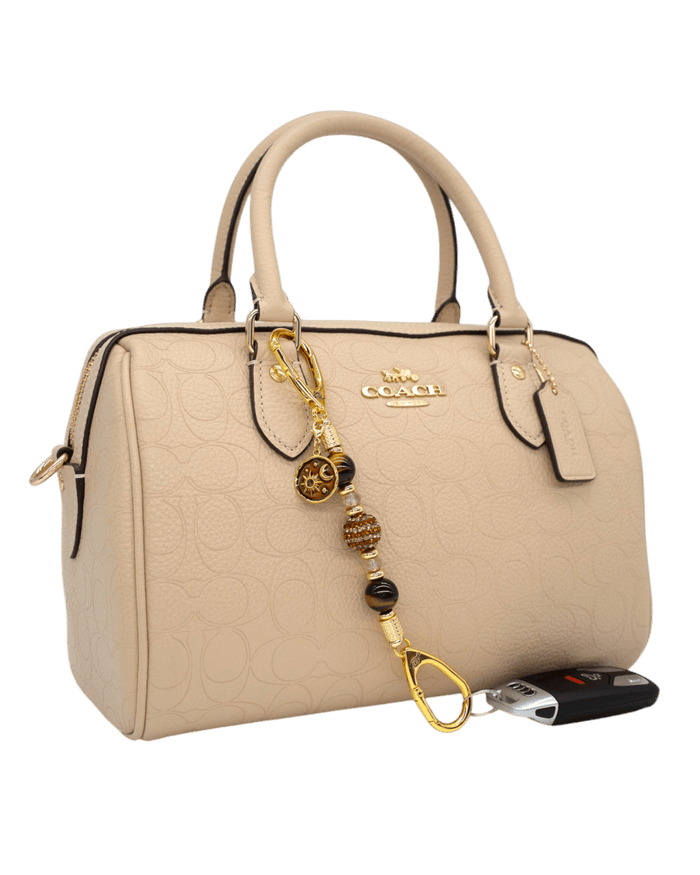 LD Keyfinder Golden Equinox-Mini accessory with Tiger Eye beads and sun and moon charm attached to a beige handbag.