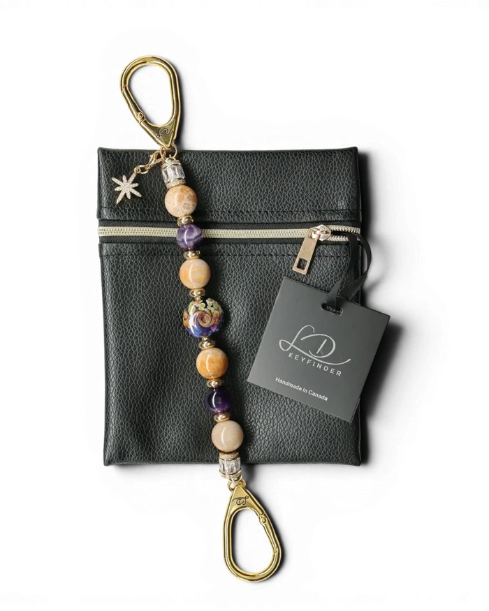 LD Keyfinder Golden Nebula keychain with purple, gold, and tan beads, a glass focal bead, and a star charm. Includes a black vegan leather pouch.
