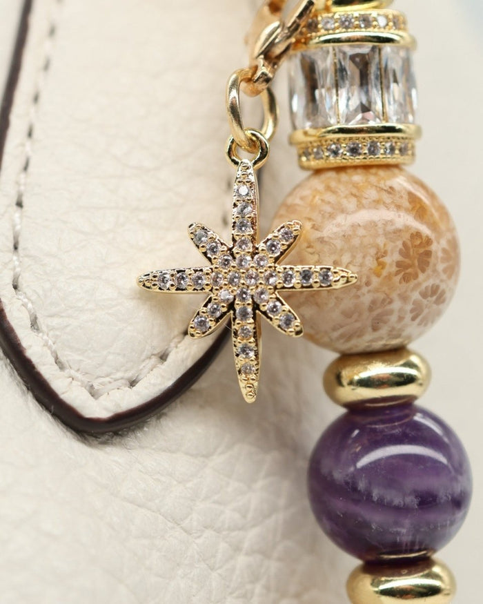 LD Keyfinder Golden Nebula charm with fossil coral, amethyst, gold spacers, and pavé star charm on a white textured surface.