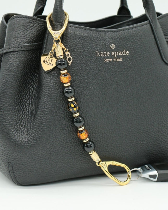 LD Keyfinder Golden Purrs beaded keychain with black obsidian, gold foil lampwork beads, and cat charms on a black bag