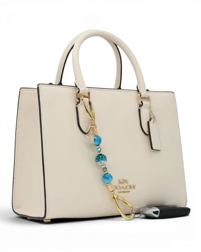 LD Keyfinder Golden Reef Mini charm with aqua hemimorphite beads, crystal, starfish, and sea turtle charms on a cream handbag.