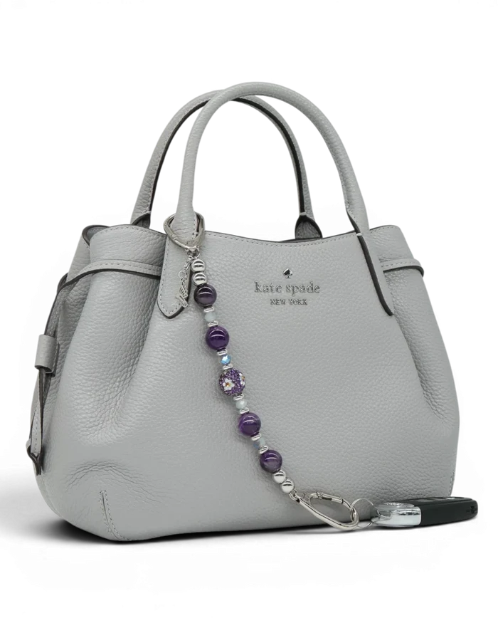 LD Keyfinder Hummingbird Dream keychain with amethyst, glass beads, and hummingbird charm attached to a grey handbag.