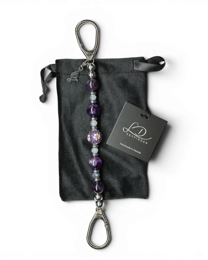LD Keyfinder Hummingbird Dream keychain with amethyst, crystal daisy bead, and hummingbird charm on black velvet bag.