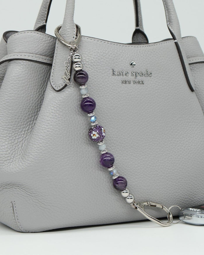 LD Keyfinder Hummingbird Dream keychain with amethyst, glass beads, and hummingbird charm on a grey handbag.