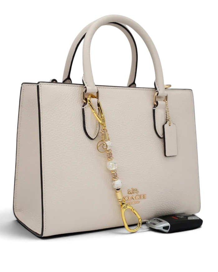 LD Keyfinder Mediterranean Glow Mini featuring Mother of Pearl, ivory shell beads, and gold charms on a cream handbag