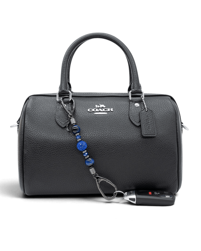 LD Keyfinder Midnight Sapphire Mini accessory with blue tiger eye and sapphire crystals attached to a black handbag
