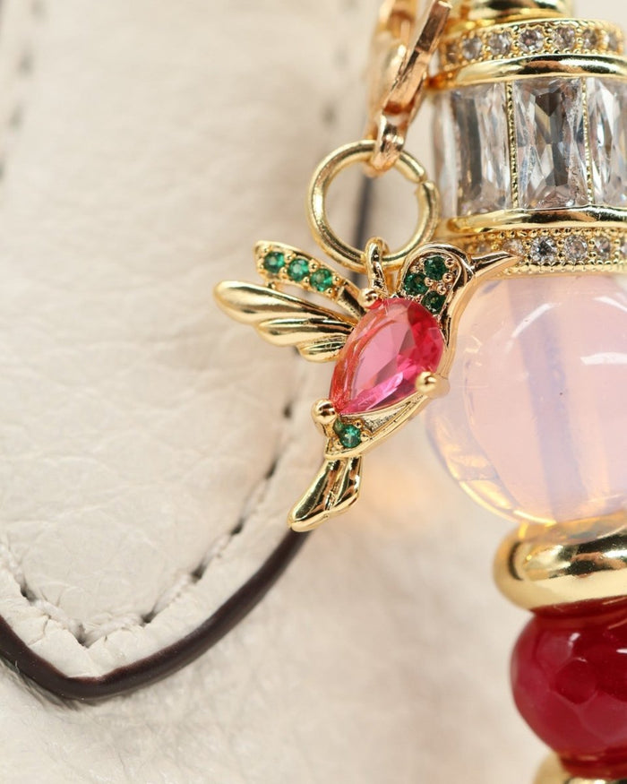 LD Keyfinder Opalite Bloom charm with hummingbird, pink opalite, ruby, and gold accents on a white textured surface.