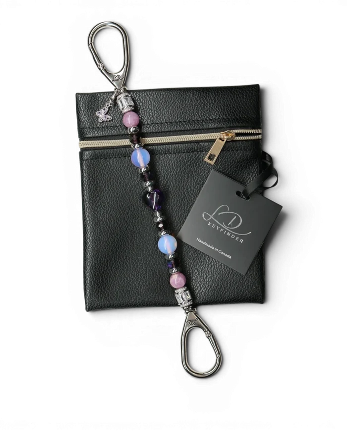 LD Keyfinder Orchid Flutter beaded accessory with lepidolite, opalite, and a butterfly charm on a black leather pouch.