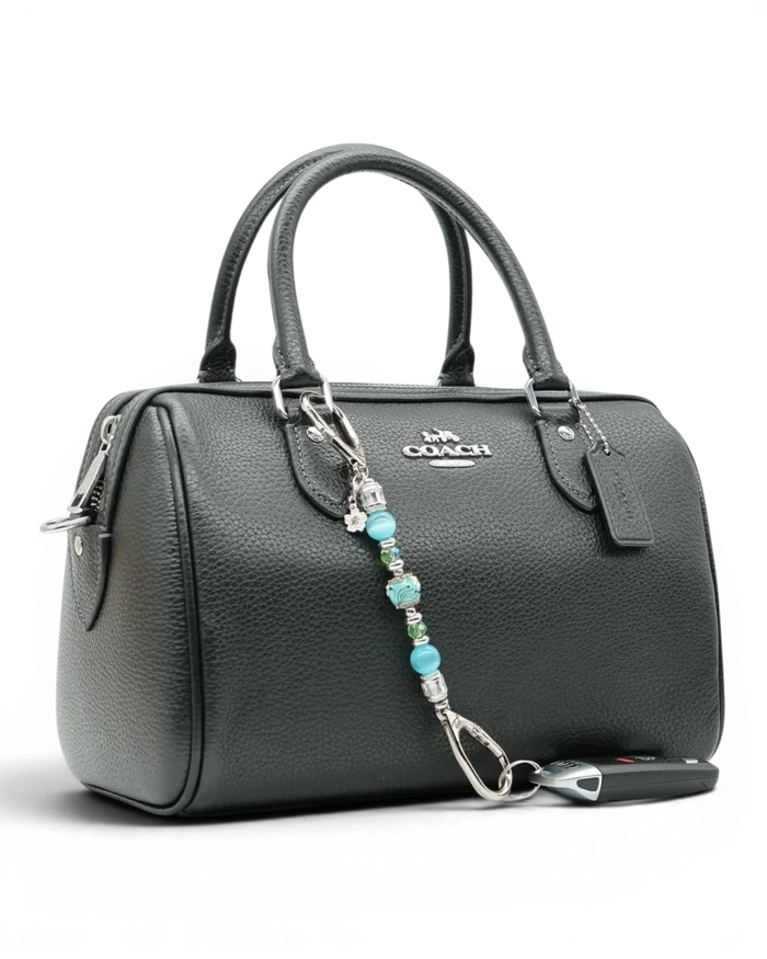 LD Keyfinder Petite Azure Meadow charm with aqua blue cat's eye beads, green glass beads, and a daisy charm attached to a black handbag.