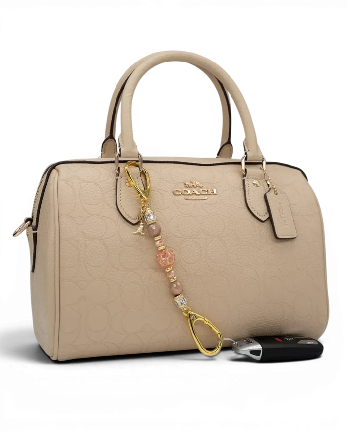LD Keyfinder Petite Birdsong Bliss beaded charm with sunstone, peach glass, and gold bird accent on a beige handbag.