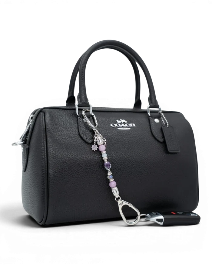 LD Keyfinder Petite Blooming Joy accessory with lavender Lepidolite and purple Jade beads attached to a black handbag.