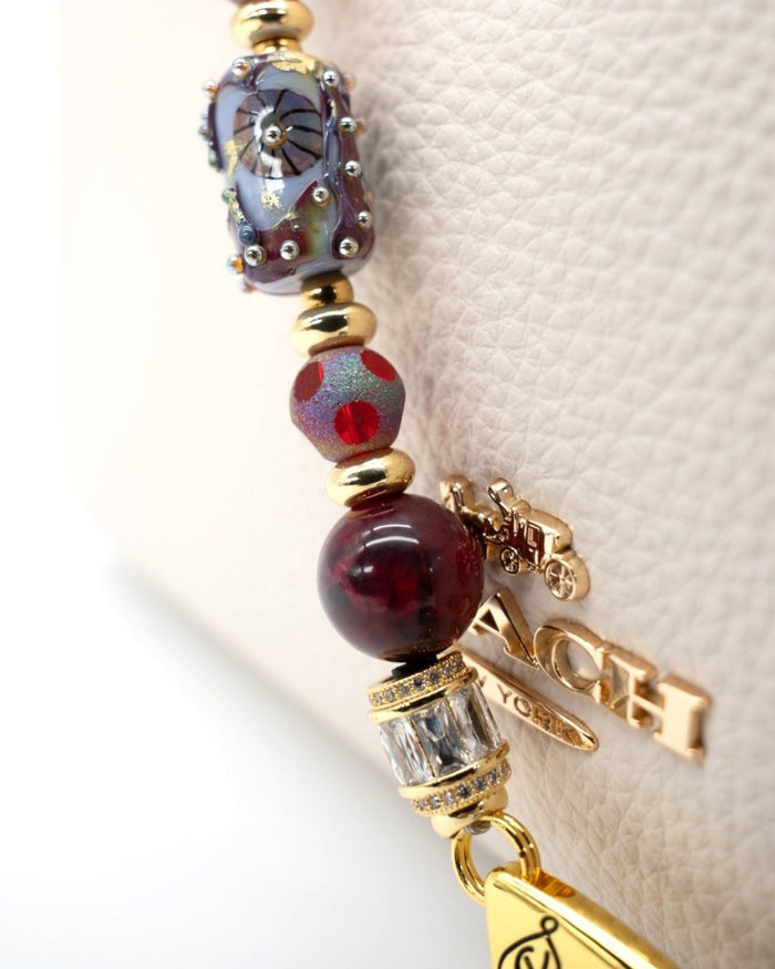 LD Keyfinder Petite Bordeaux Bloom featuring artisan glass, burgundy agate, and 18KT gold-plated accents on a handbag.