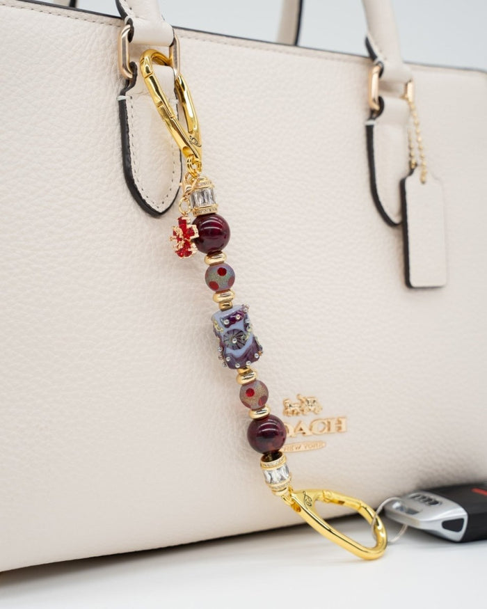 LD Keyfinder Petite Bordeaux Bloom featuring burgundy agate, artisan glass, and gold-plated accents on a cream handbag