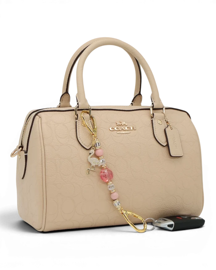 LD Keyfinder Petite Flamingo Fantasy accessory with pink opal beads and gold flamingo charm attached to a beige bag.