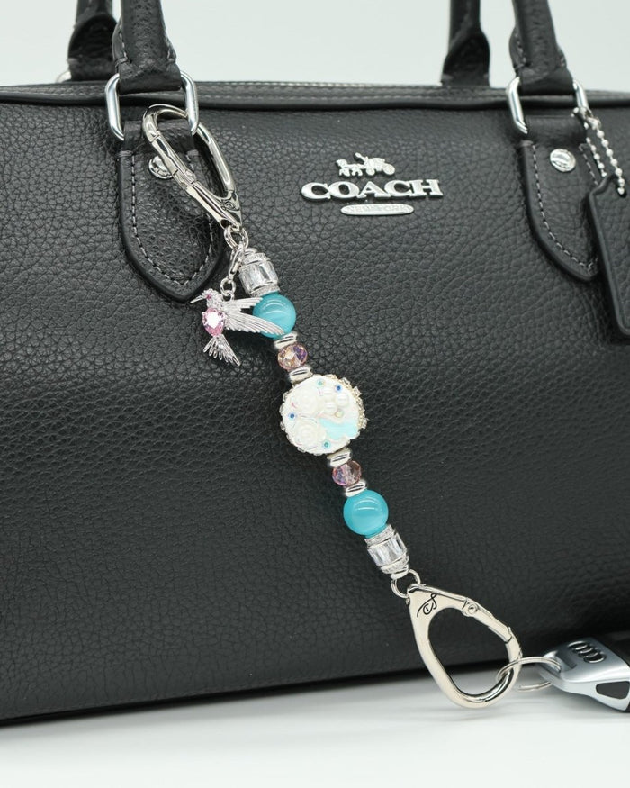 LD Keyfinder Petite Garden Serenade accessory with aqua beads, pink glass, and a hummingbird charm on a black handbag.