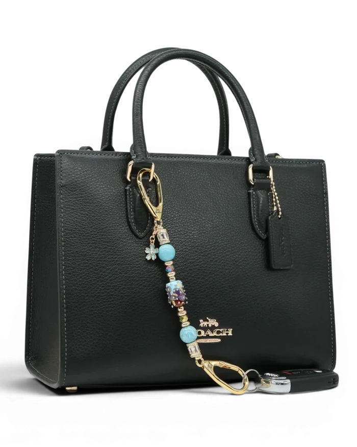 LD Keyfinder Petite Gilded Fantasy keychain with blue glass bead, gold leaf, larimar, and flower charm on black bag.