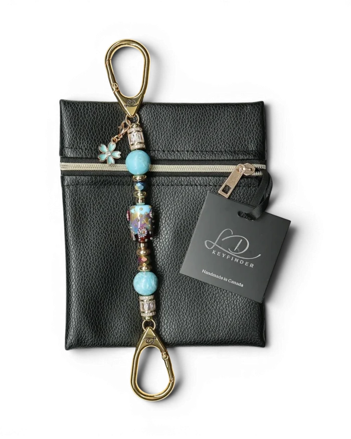 LD Keyfinder Petite Gilded Fantasy keychain with blue glass art bead, larimar, gold-plated accents, and flower charm on black pouch.