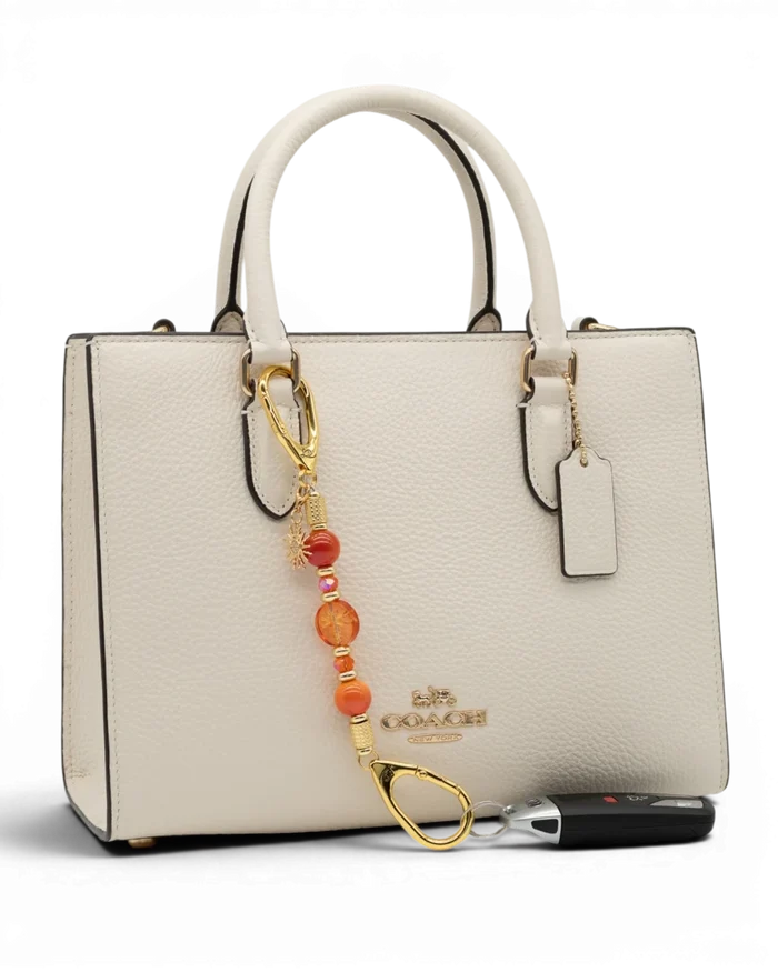 LD Keyfinder Summer Sunset Mini beaded accessory with coral glass, agate beads, and gold sun charm on a white handbag.