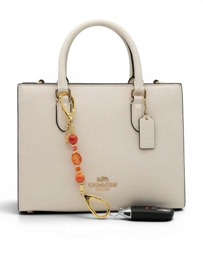 LD Keyfinder Summer Sunset Mini beaded accessory with coral glass, agate, and gold sun charm on a white handbag.