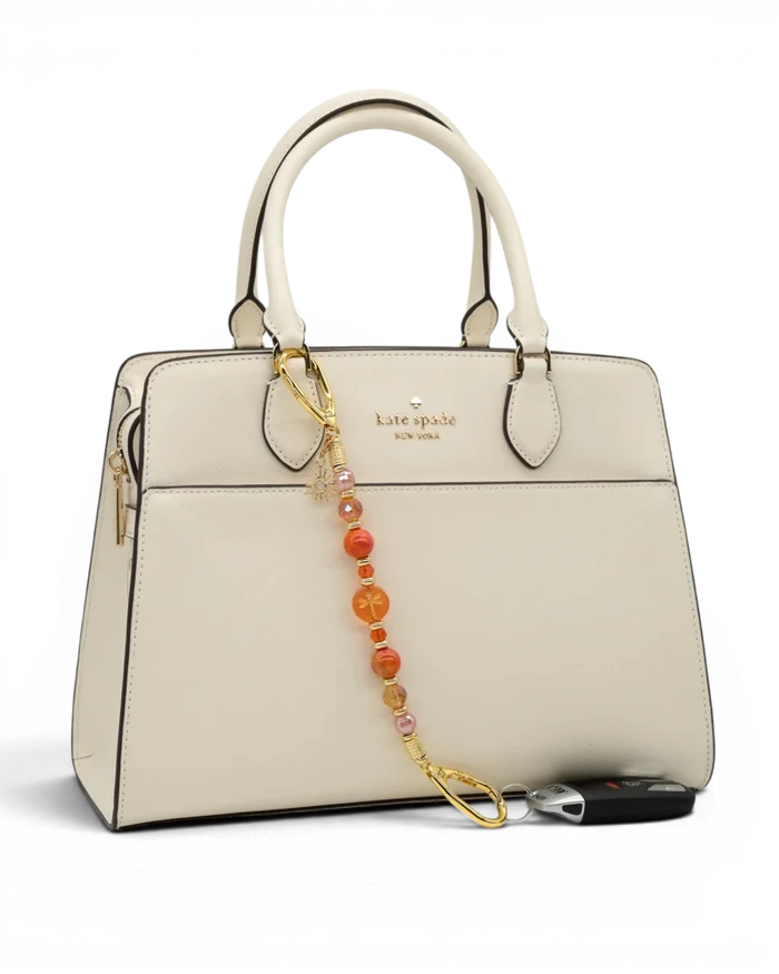 LD Keyfinder Summer Sunset beaded keychain with coral glass, cherry quartz, and gold sun charm attached to a cream bag