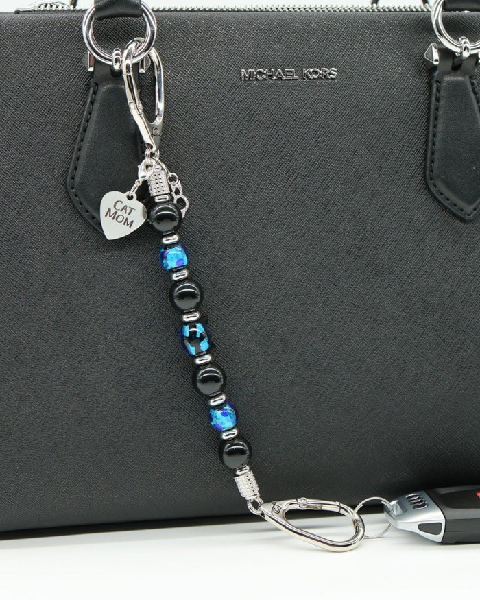LD Keyfinder Whisker Dreams beaded keychain with black obsidian, blue lampwork glass, and Cat Mom charm on a handbag.
